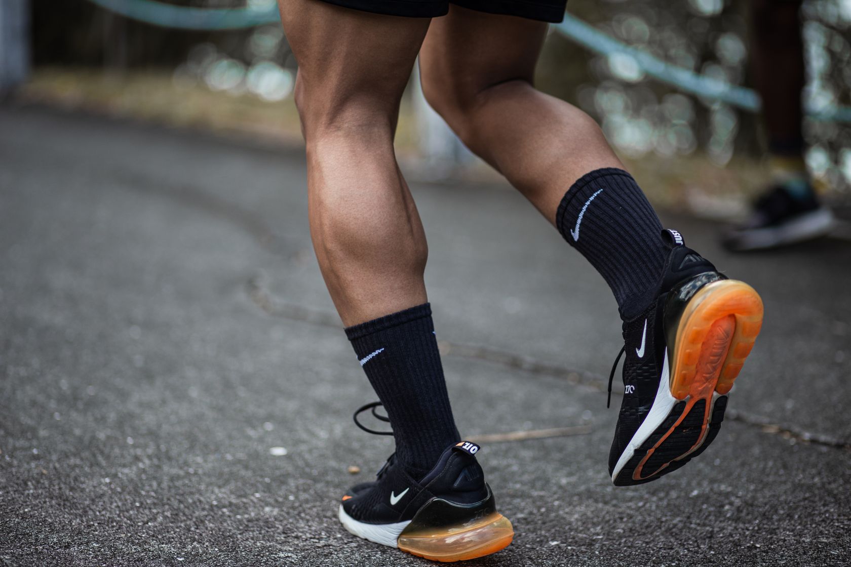 Close-up from behind of a person's calves in black socks and running shoes on a paved path