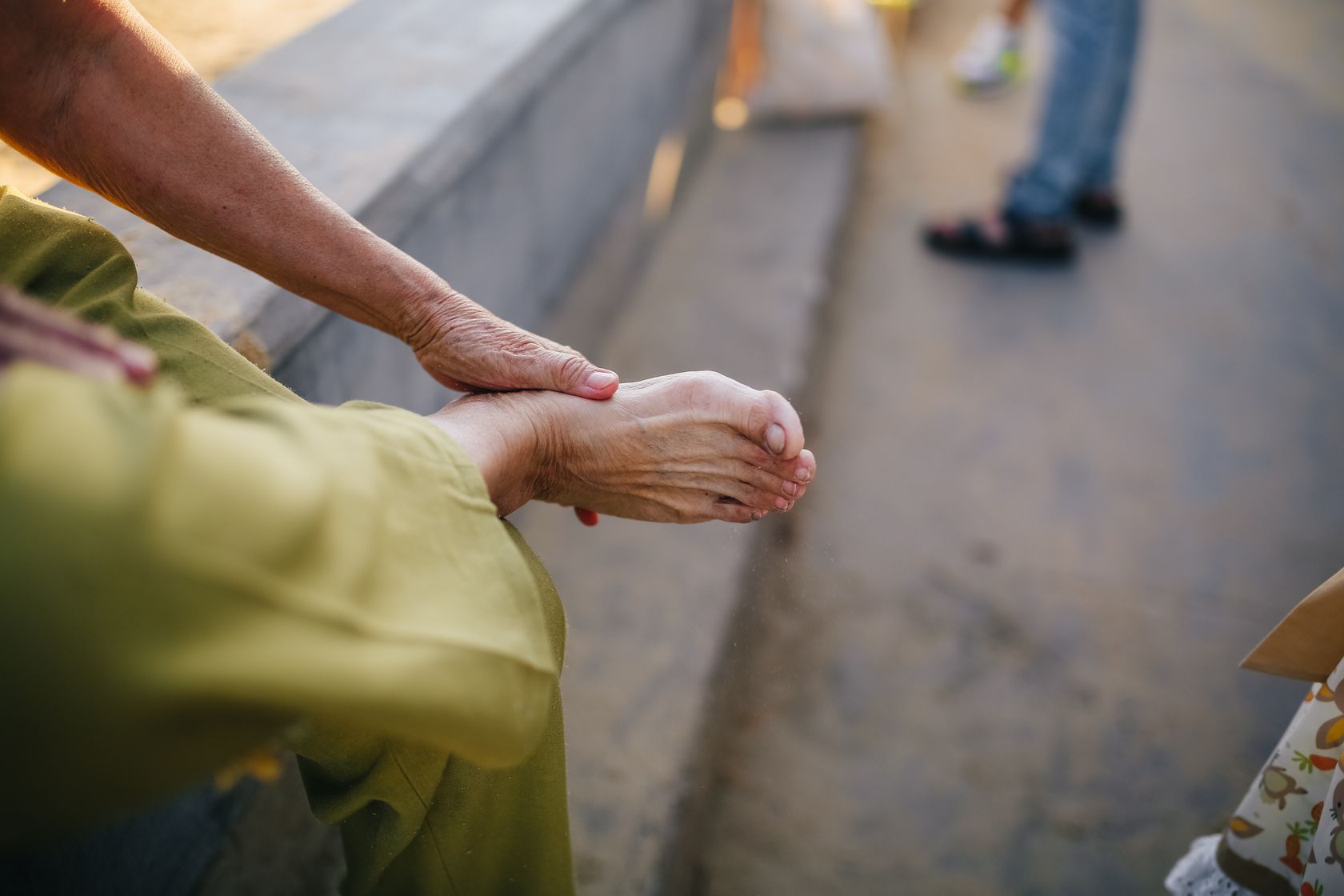 Close-up of a seated person holding their bare foot near the ankle outdoors